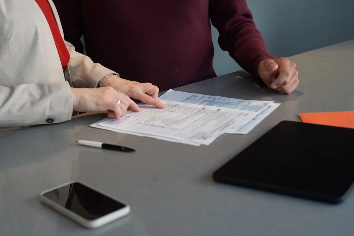 Deux personnes penchées sur un document imprimé, l’une pointant du doigt une ligne d’un tableau de données.